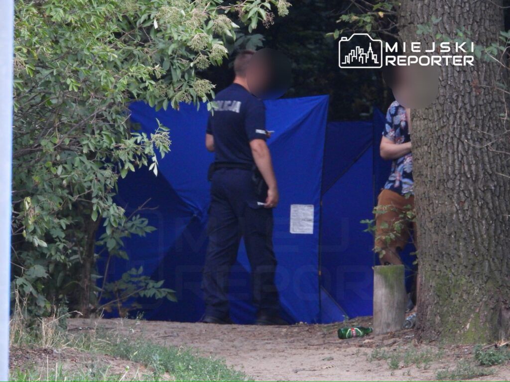 Policjant rozmawia z mężczyzną przy niebieskim namiocie w leśnej okolicy. W tle widoczne śmieci.