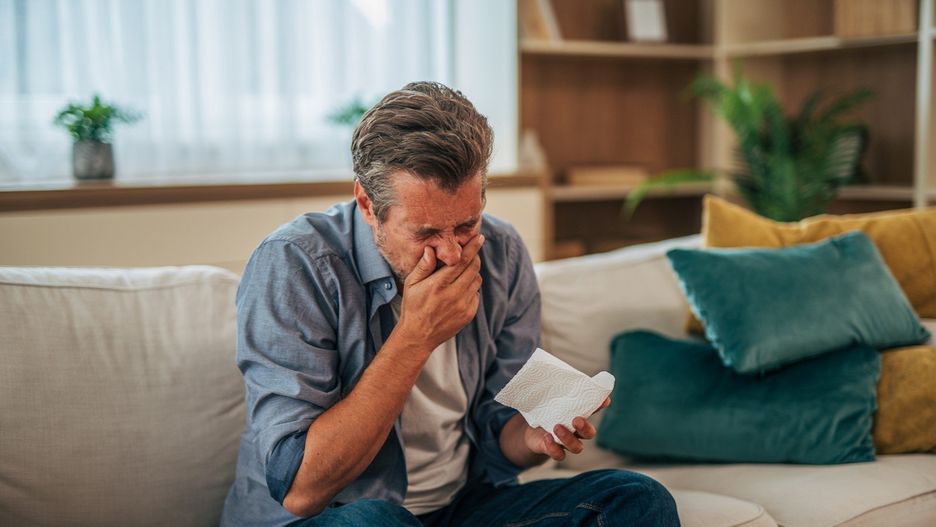 Mature man coughing and feeling sick on the sofa at home