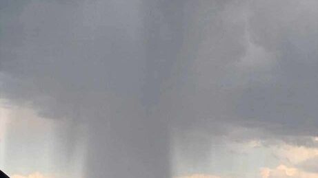 Intensywne opady deszczu spływające z chmur nad domami w podmiejskim krajobrazie.