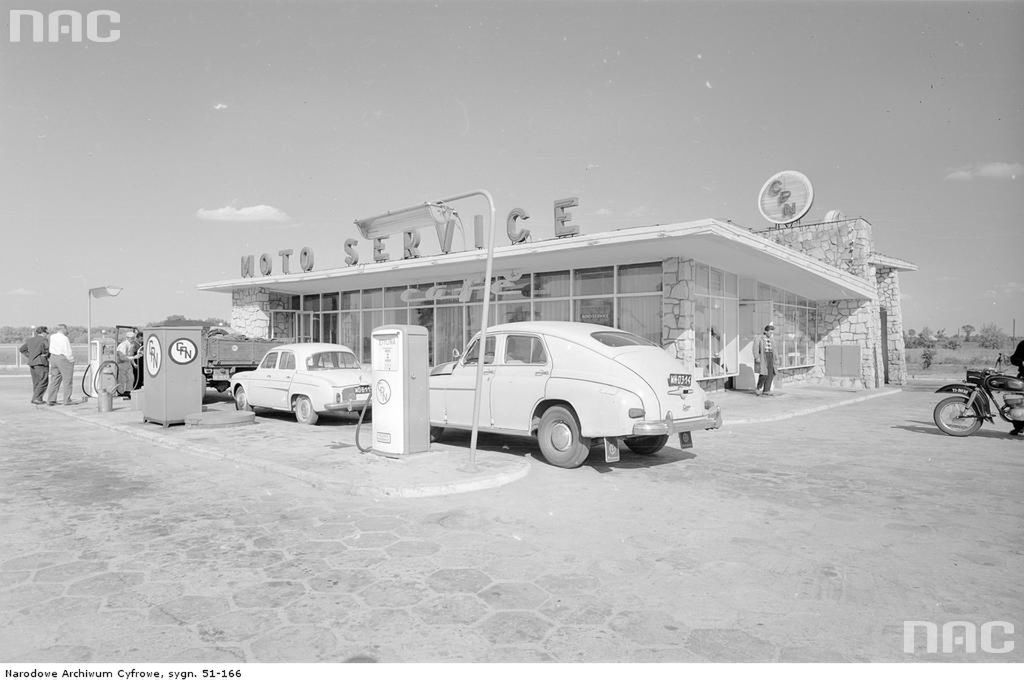 Stacja benzynowa Centrali Produktów Naftowych w Jankach. Widok zewnętrzny budynku stacji. Widoczne dystrybutory paliwa oraz samochody osobowe - z prawej Warszawa M-20 model 57, z lewej Renault Dauphine.