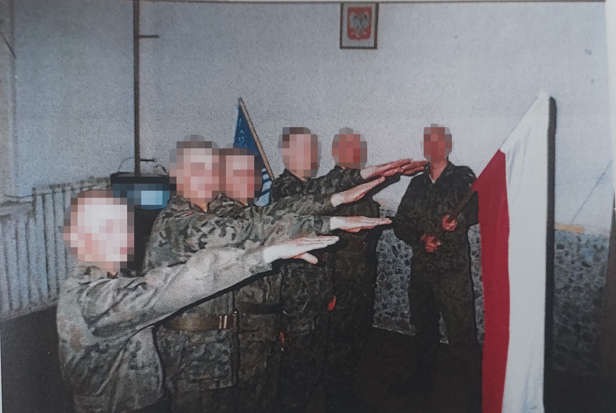 Dominik G. ps. Grucha trzyma flagę, do której hajlują koledzy.