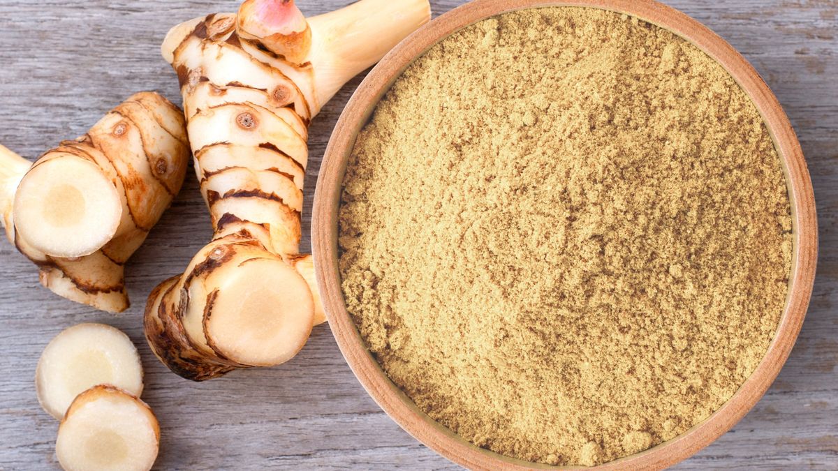 Alpinia galanga powderAlpinia galanga powder in wooden bowl and fresh galangal rhizome  isolated on wooden table background. Top view.Everyday better to do everything