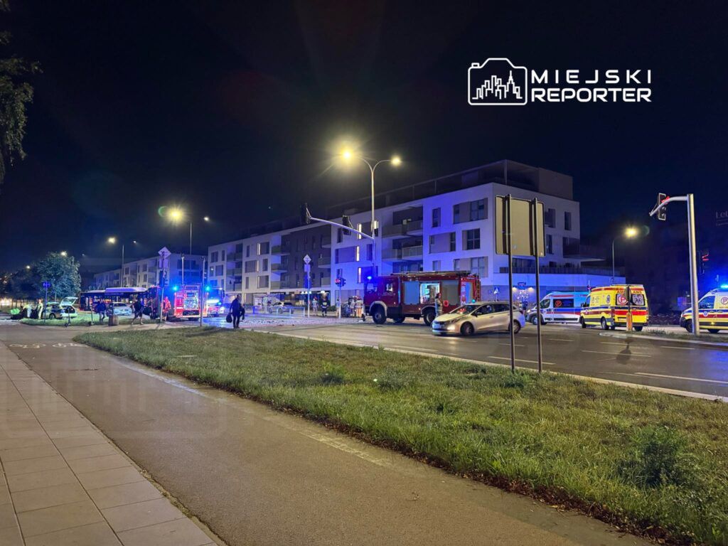 Na ulicy w nocy, służby ratunkowe, w tym straż pożarna i karetki, interweniują przy wypadku drogowym.