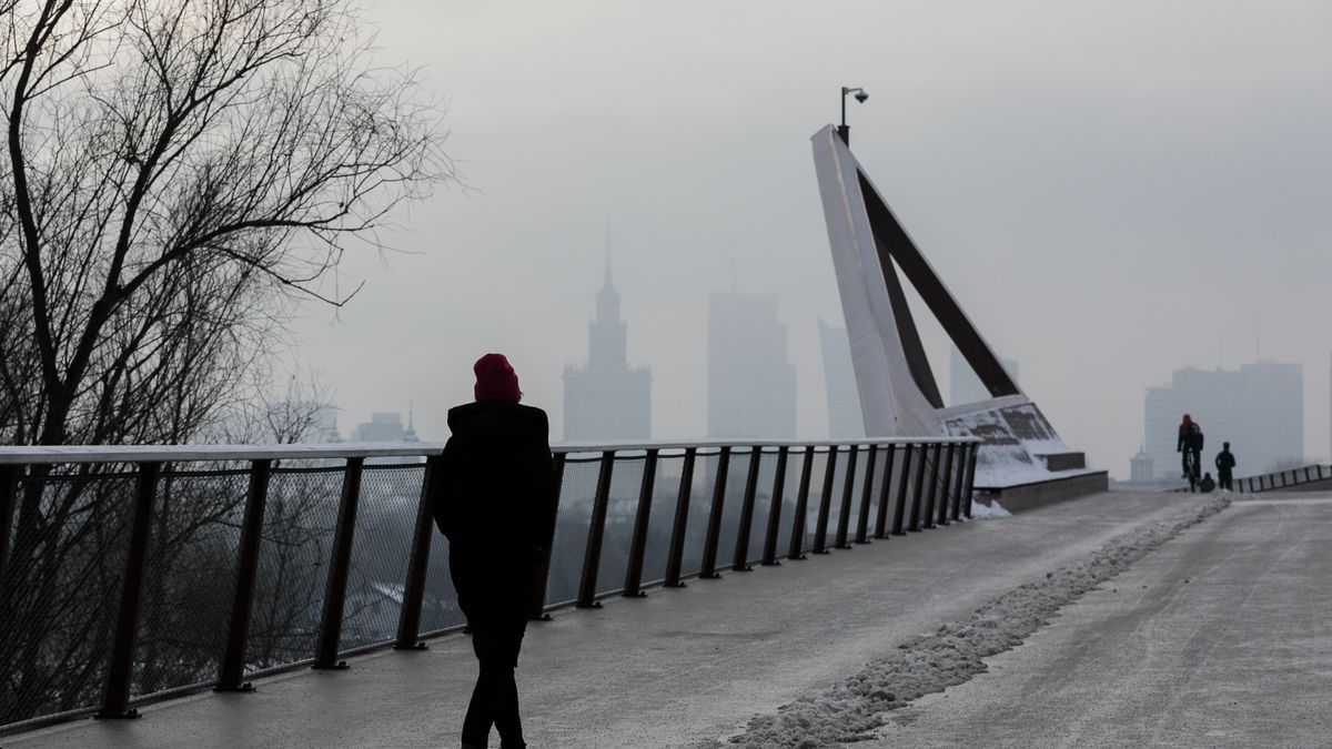 WARSAW, POLAND - 2026/01/08: People walk across a pedestrian and bicycle bridge over the Vistula on a cold day, with winter haze covering the city skyline in the background. Freezing temperatures and heavy snowfall in early January led to a surge in domestic heating, increasing emissions from solid fuel furnaces across the region. At the same time, stagnant weather conditions trapped pollutants near the ground, causing particulate matter levels to rise sharply. As a result, city officials issued smog alerts as thick haze covered the Warsaw skyline. (Photo by Volha Shukaila/SOPA Images/LightRocket via Getty Images)