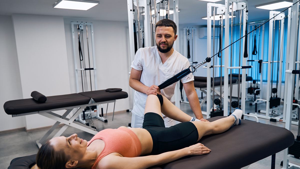 Young woman training leg muscles and joints under doctors supervision on massage tableYoung woman training leg muscles and joints under doctors supervision on massage table in rehabilitation center. Male physical therapist assists patient in recovery from sports injury. Rehab clinicrecovery, woman, close up, therapist, young, doctor, male, physical, therapy, patient, rehabilitation, massage, medical, foot, correction, equipment, people, man, leg, center, osteopath, treatment, rehab, physiotherapy, knee, clinic, muscles, injury, spine, supervision, fitness, table, joint, sport, health, medicine, Caucasian, trauma, care, bandage, orthopedic, sprain, disease, gymnastics, body, regeneration, injured, bone, osteoporosis