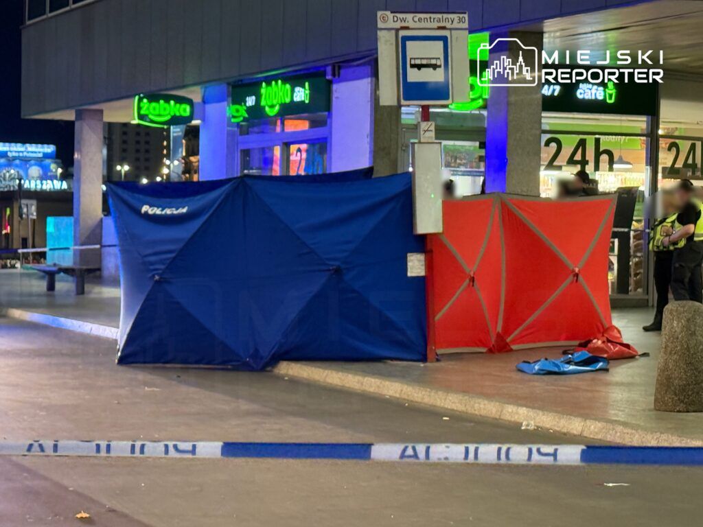 Policjanci zabezpieczają miejsce zdarzenia, gdzie rozłożone są niebieskie i czerwone namioty, obok sklepu Żabka.