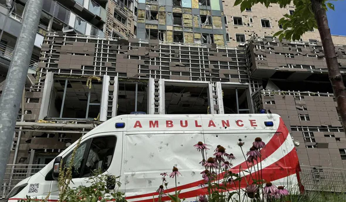 A damaged ambulance in front of the destroyed hospital building