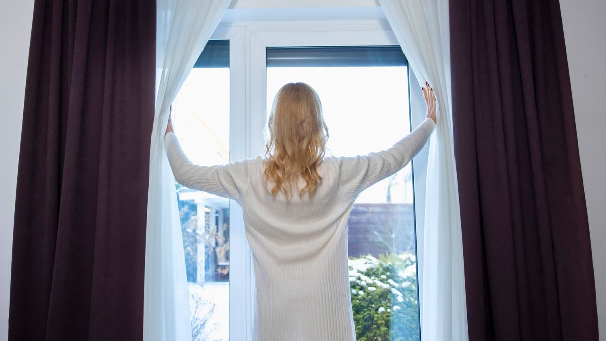 Kobieta odsłania białe firanki