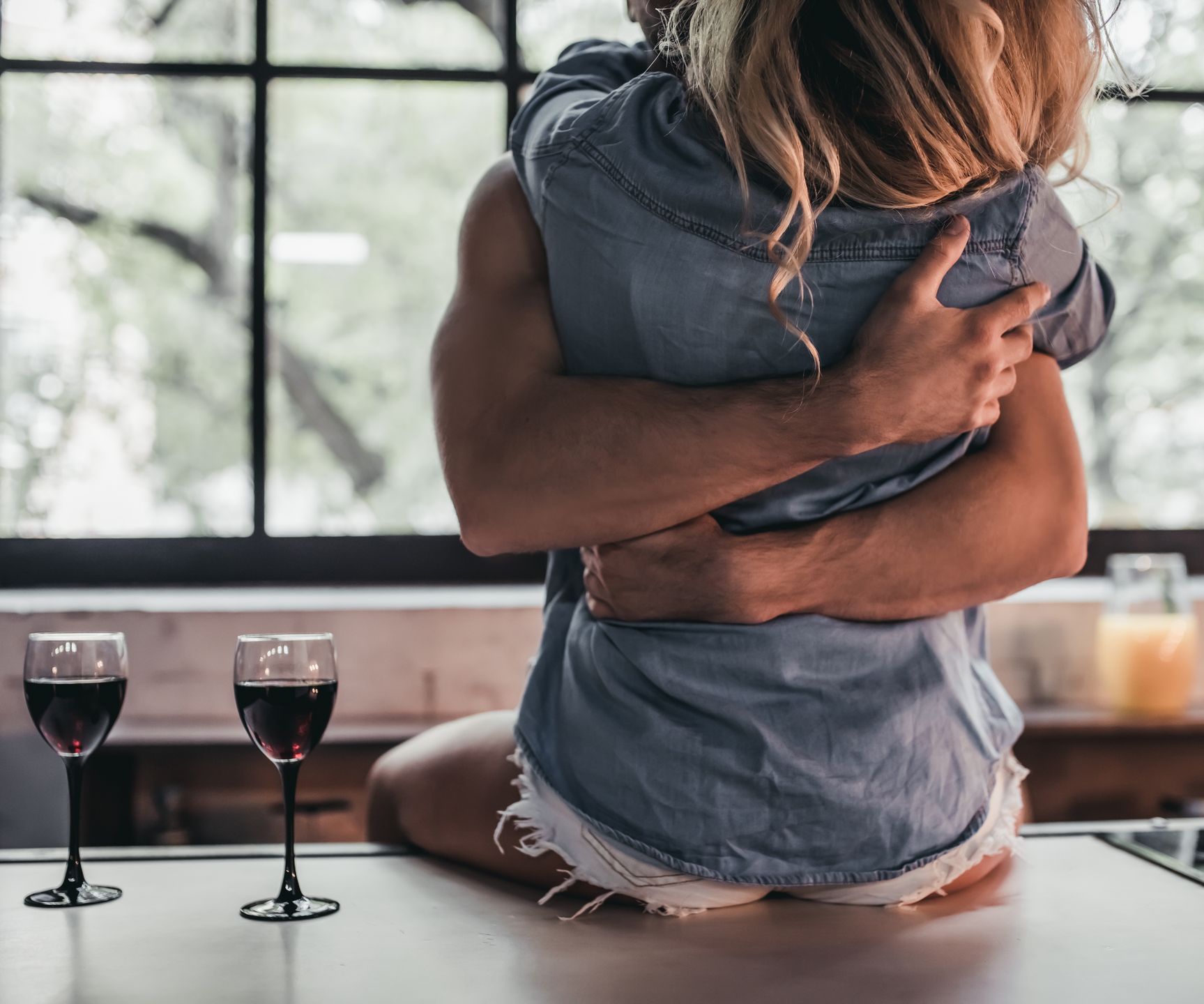 Cropped image of attractive passionate couple on kitchen. Man hugs woman while she's sitting on table.