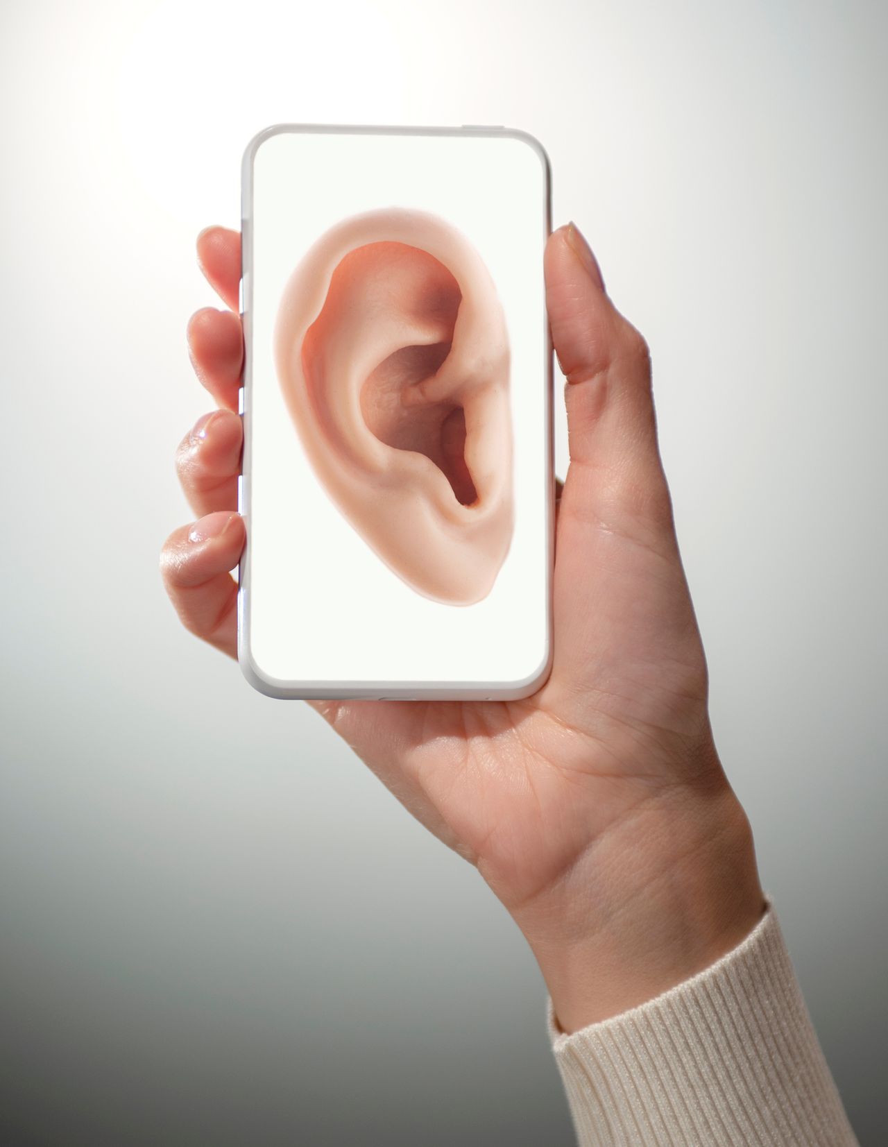 Young woman’s hand holding a smart phone with a close-up of human ear on it