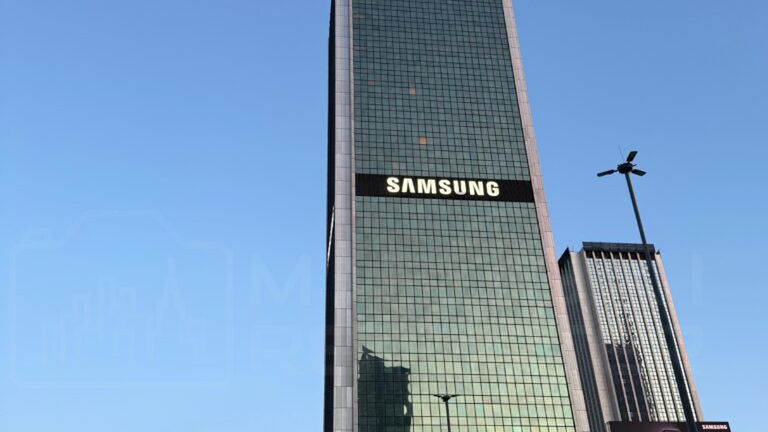 Nowoczesny wieżowiec z przeszkloną fasadą, z logo "Samsung" i "Presidential" na górze, otoczony ludźmi na ulicy.