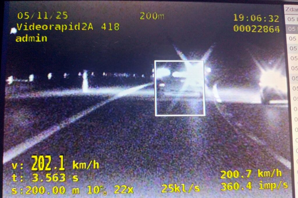 Pojazd poruszający się z prędkością 202,1 km/h na ciemnej drodze, z widocznymi śladami świetlnymi.