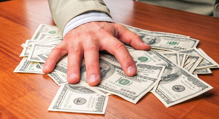Zdjęcie przedstawia rękę trzymającą pieniądze - symbol chciwości 