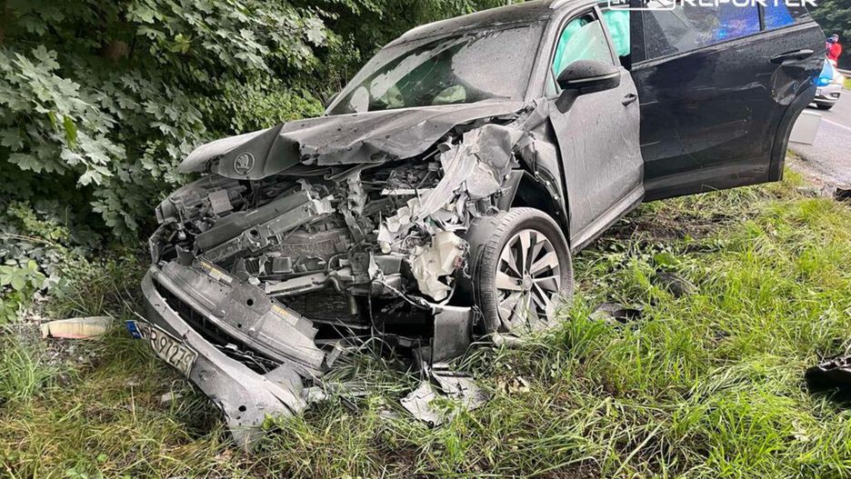 Zniszczony samochód osobowy stoi na poboczu drogi, obok gęstej roślinności.