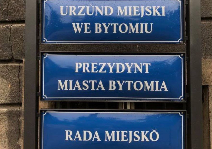 Śląskie. Na budynku Urzędu Miejskiego w Bytomiu zawisły flagi województwa śląskiego, a przed wejściem do budynku tabliczki urzędowe po śląsku.