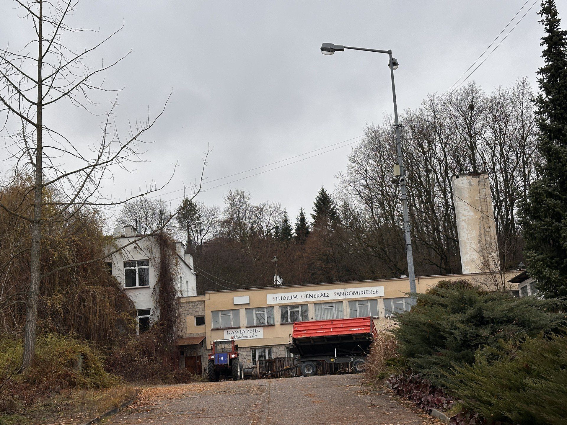 To prawie dwuipółhektarowa działka z budynkiem dydaktycznym i wolnostojącym mniejszym obiektem, garaże, parking, arboretum oraz droga dojazdowa.