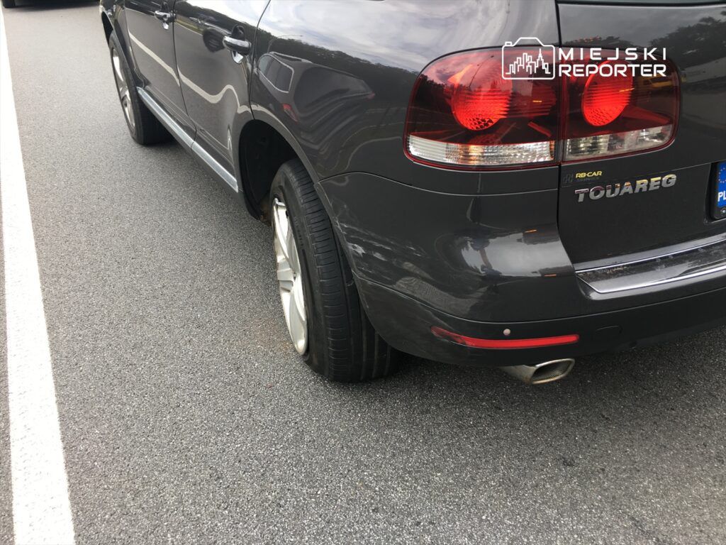 Samochód terenowy marki Volkswagen Touareg z uszkodzoną oponą zaparkowany na asfaltowej drodze.