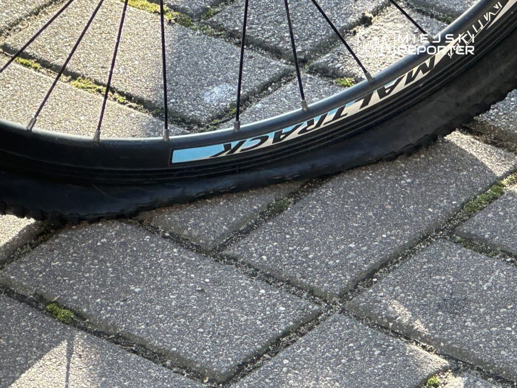 Płaska opona rowerowa leży na kostce brukowej, z widocznymi detalami obręczy i szprych.