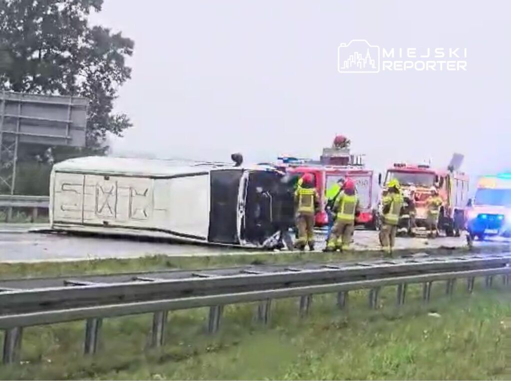 Czterech strażaków w mundurach ratunkowych pracuje przy przewróconym samochodzie dostawczym na poboczu drogi.