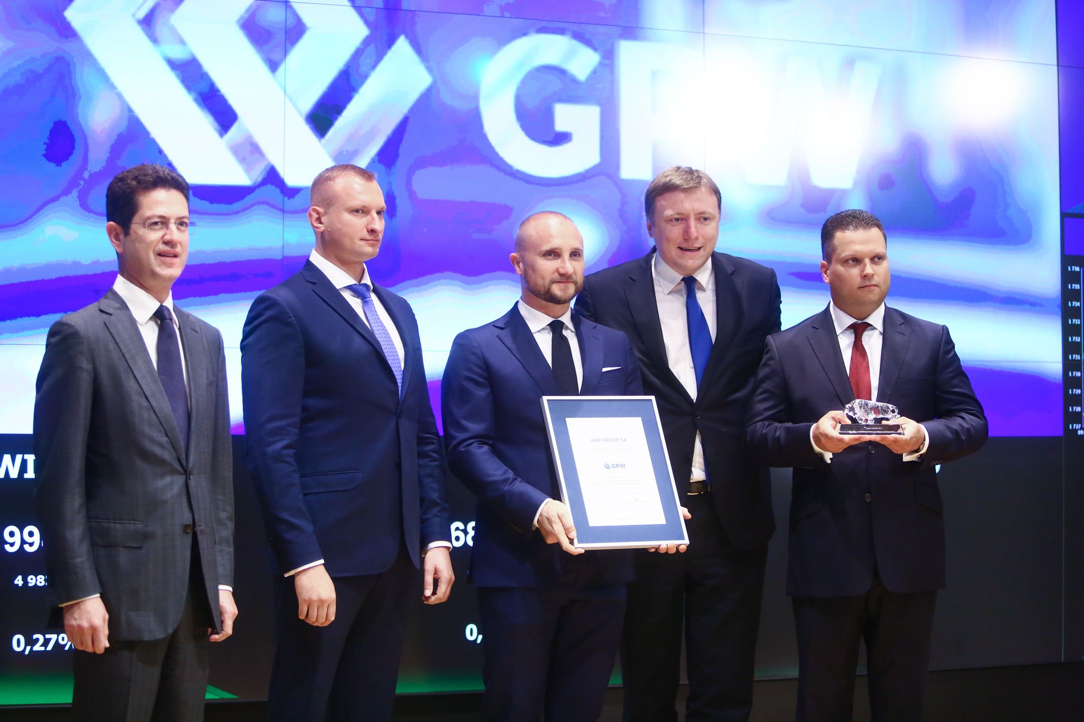 Debiut ASM Group na GPW. Od lewej (funkcje według stanu na 2016 r.): członek zarządu ASM Group S.A. Rossen Hadjiev, członek zarządu ds. finansowych ASM Group S.A. Jacek Pawlak, prezes zarządu ASM Group S.A. Adam Stańczak, Paweł Dziekoński (wówczas GPW), wiceprezes zarządu ASM Group S.A., Marcin Skrzypiec 