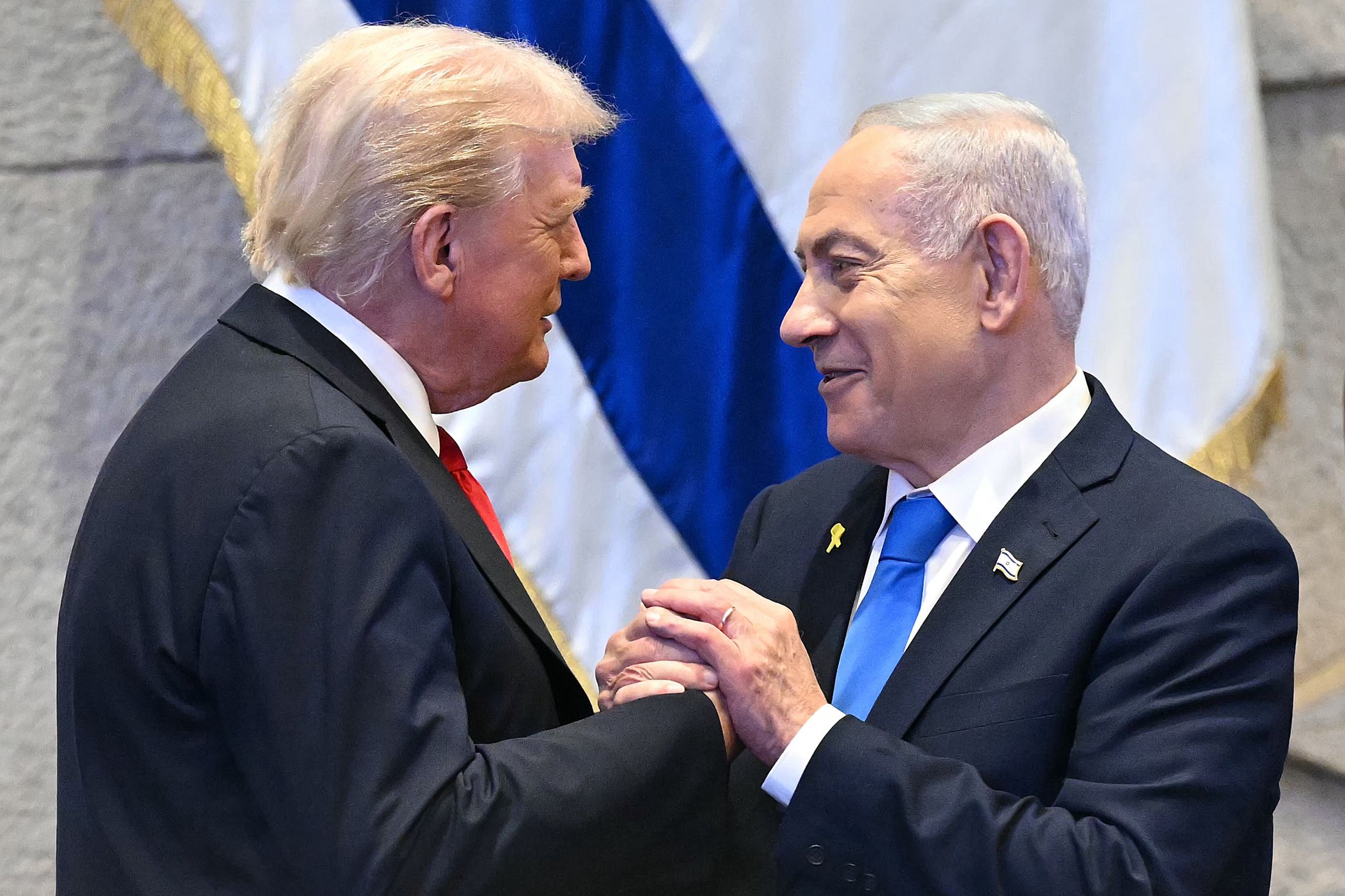 JERUSALEM - OCTOBER 13: U.S. President Donald Trump (L) holds hands and speaks with Israeli Prime Minister Benjamin Netanyahu at the Israeli parliament, the Knesset, on October 13, 2025 in Jerusalem. President Trump is visiting the country hours after Hamas released the remaining Israeli hostages captured on Oct. 7, 2023, part of a US-brokered ceasefire deal to end the war in Gaza. (Photo by Saul Loeb - Pool/Getty Images)