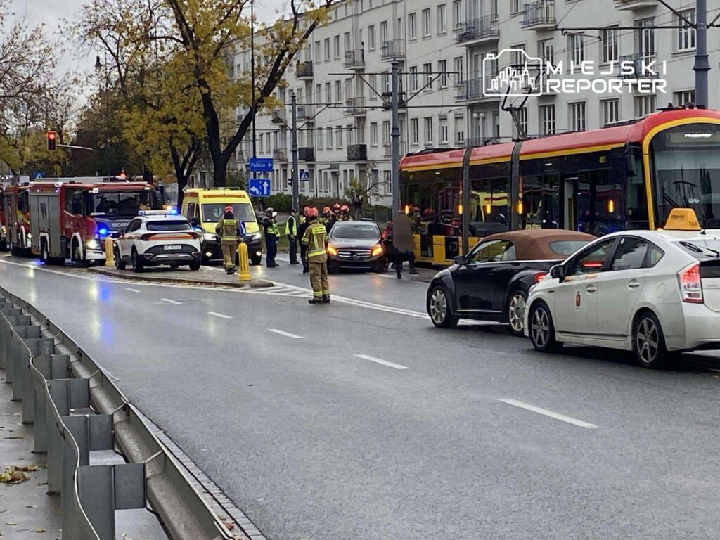 Na ulicy zatrzymane pojazdy, w tym wóz strażacki i karetka, podczas interwencji służb ratunkowych.