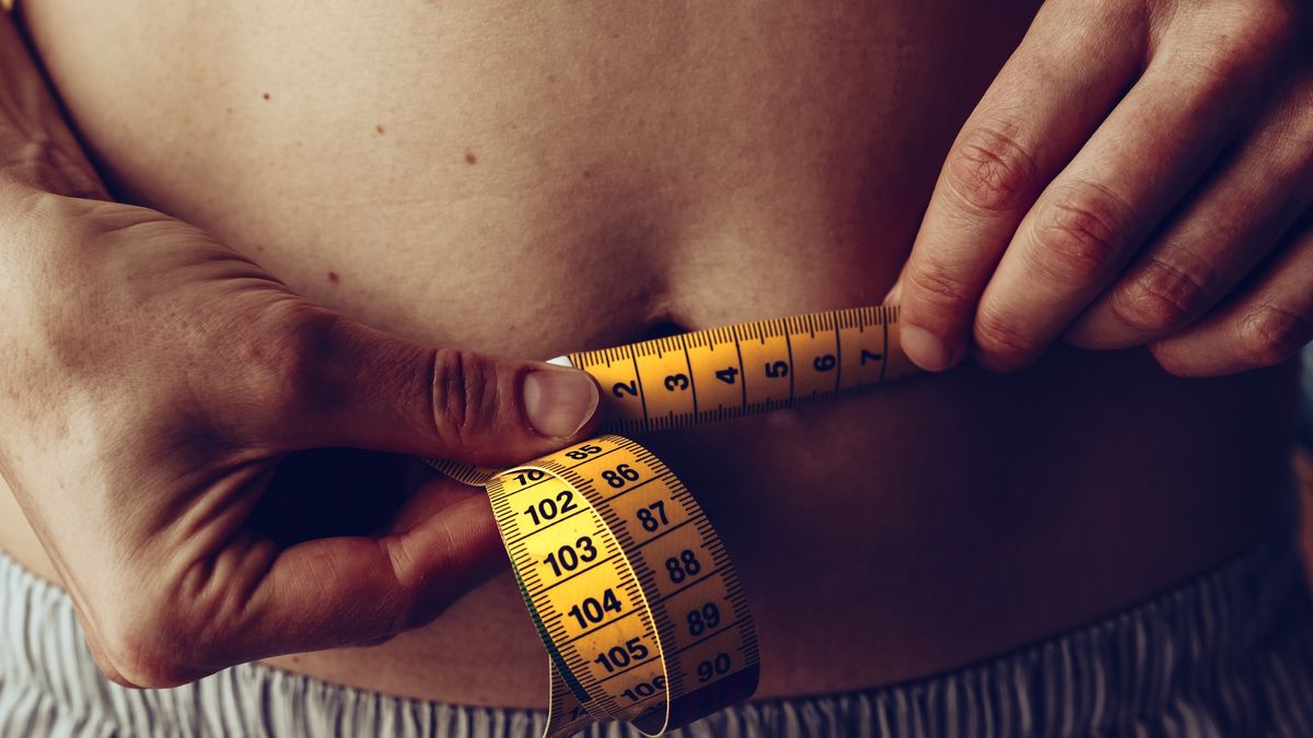 An unrecognizable woman uses a tape measure with both hands to measure the belly circumference.Oliver Helbig