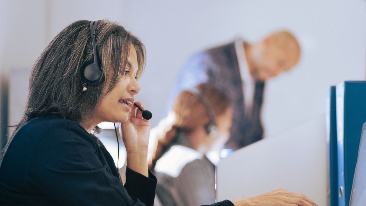Businesswoman with headset talking to caller in customer services department. Female executive with a headset working on a laptop in call center office.
