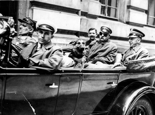 Warszawa. Na tylnym siedzeniu samochodu siedzą Józef Piłsudski (po lewej stronie, w goglach), mjr Konrad Zembrzuski (z prawej) i pies "Pies". Samochód prowadzi szofer Zygmunt Malinowski, obok niego siedzi wachmistrz Walenty Wójcik.