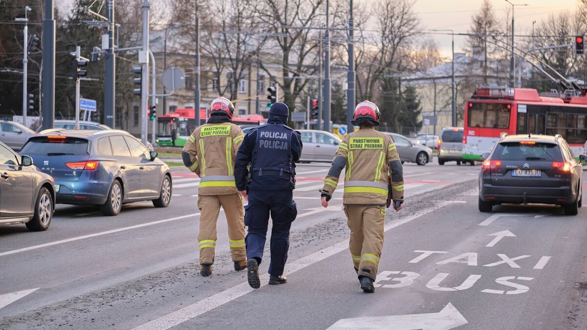 Dwóch strażaków i policjant idą wzdłuż ścieżki z betonu na jezdni