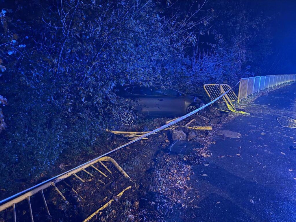 Samochód osobowy wjeżdżający w krzaki obok drogi, otoczony przez policyjne taśmy i oświetlenie.