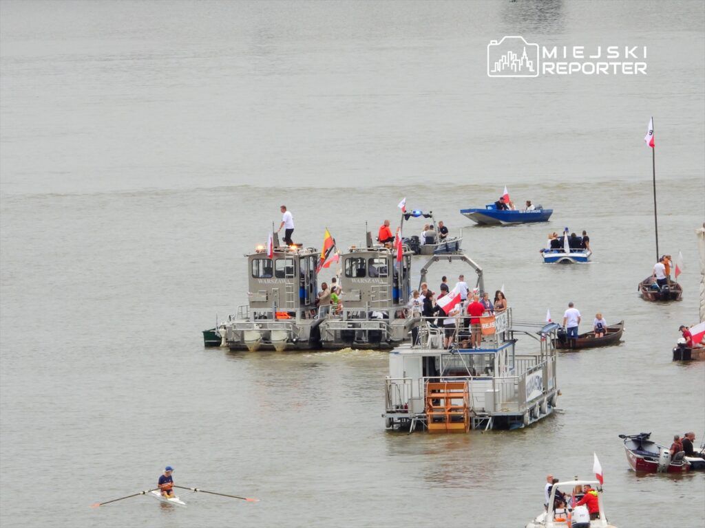 Grupa ludzi na różnych łodziach, w tym motorowych i wiosłowych, uczestniczy w wydarzeniu wodnym na rzece.