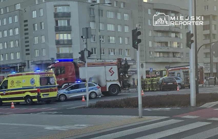 Na skrzyżowaniu stoją karetka pogotowia, radiowóz i wóz strażacki, a ratownicy prowadzą działania.