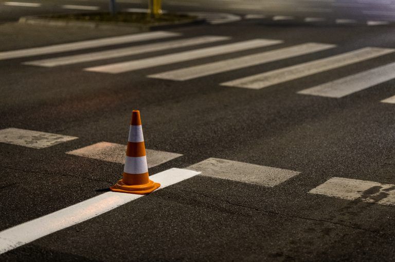 Pomarańczowy stożek drogowy umieszczony na przejściu dla pieszych na ciemnej nawierzchni ulicy.