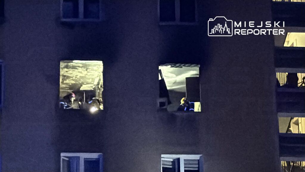 Ratownicy w hełmach pracują w oświetlonym pomieszczeniu na wyższym piętrze budynku mieszkalnego.