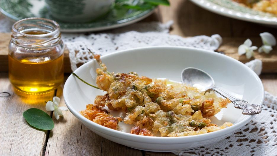 Robinia fritters served with tea and honey on a wooden table. Rustic style.