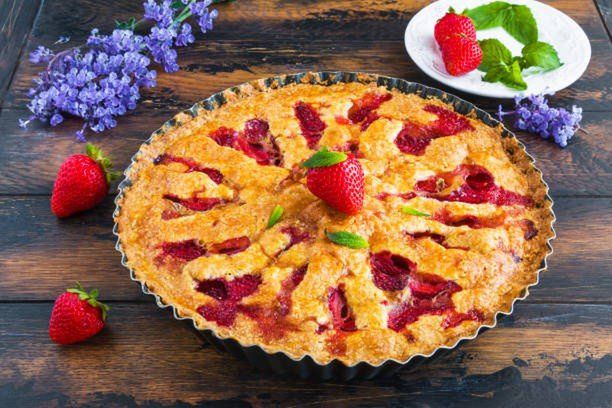Homemade summer strawberry crunchy pie in a black baking pan on the wooden rustic table.