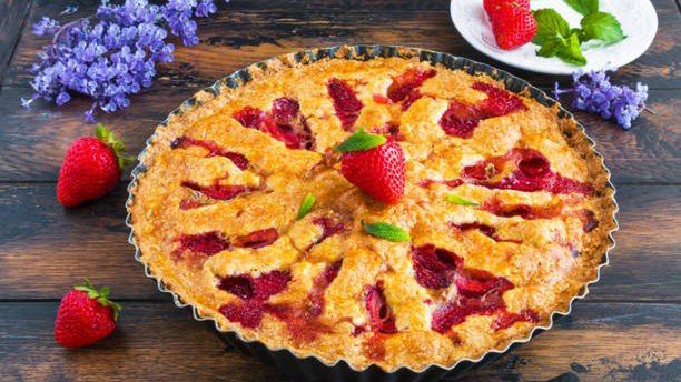Homemade summer strawberry crunchy pie in a black baking pan on the wooden rustic table.