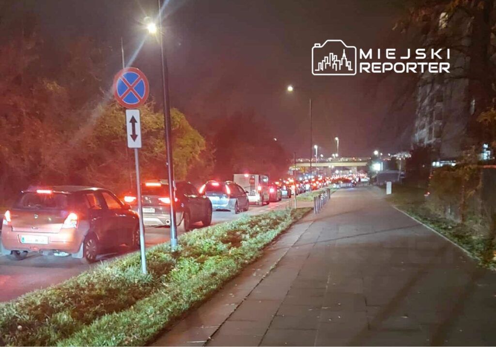 Ruch samochodowy zatrzymany w nocy na ulicy, z widocznymi światłami tylnymi pojazdów w kolejce.