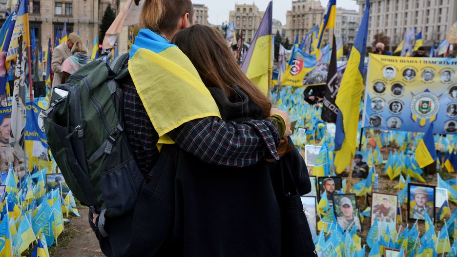 KYIV, UKRAINE - 2024/10/01: A couple of people wrapped in the Ukrainian flag stand among the flags near a makeshift memorial to fallen Ukrainian soldiers in Kyiv. Today, Ukraine honors every soldier, volunteer, doctor, everyone who in their place contributes to the defense of Ukraine. At 9:00 a.m. there was a nationwide minute of silence, and traffic was stopped for approximately 10 minutes. (Photo by Aleksandr Gusev/SOPA Images/LightRocket via Getty Images)