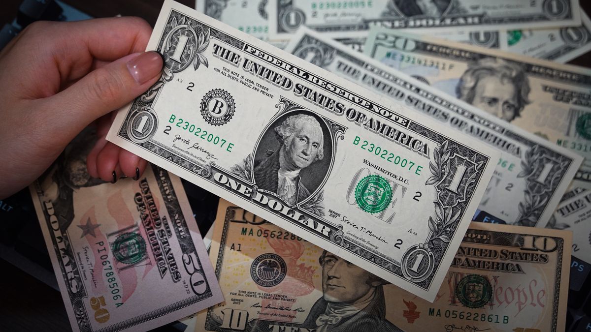 SHANGHAI, CHINA - 2024/08/31: In this illustration, a person is holding some US dollar cash bills in his hands, some of which are placed on a table. (Photo Illustration by Sheldon Cooper/SOPA Images/LightRocket via Getty Images)