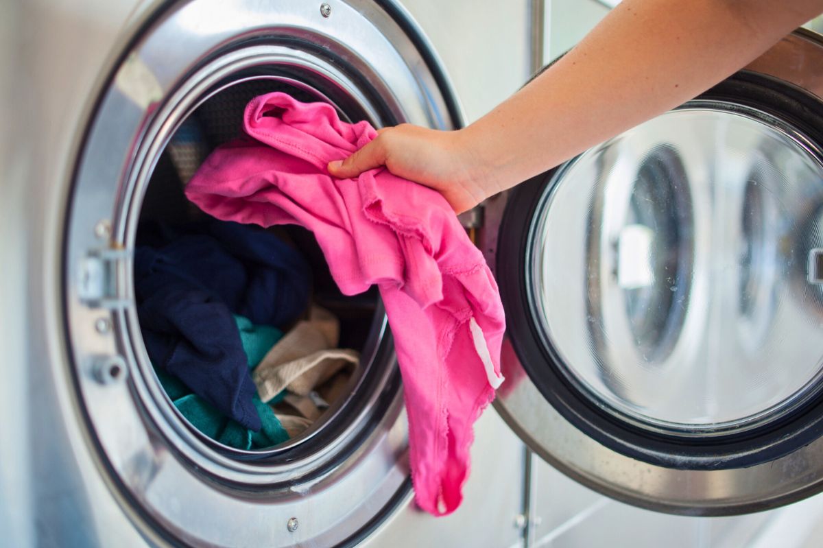 The woman puts clothes into the washing machine.