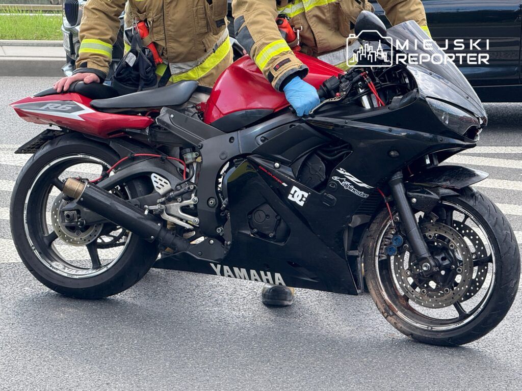 Strażak w mundurze trzyma uszkodzony motocykl marki Yamaha R6 przy krawężniku na miejskiej ulicy.