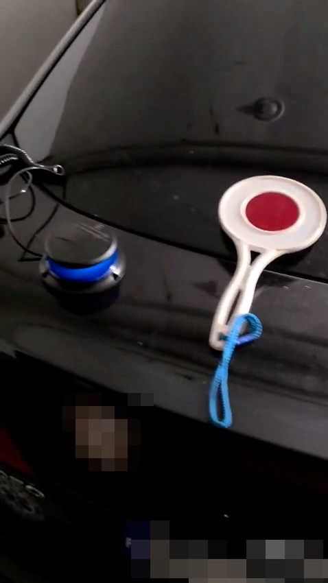 Na czarnej powierzchni samochodu leży niebieski głośnik oraz biała paletka z czerwoną końcówką.