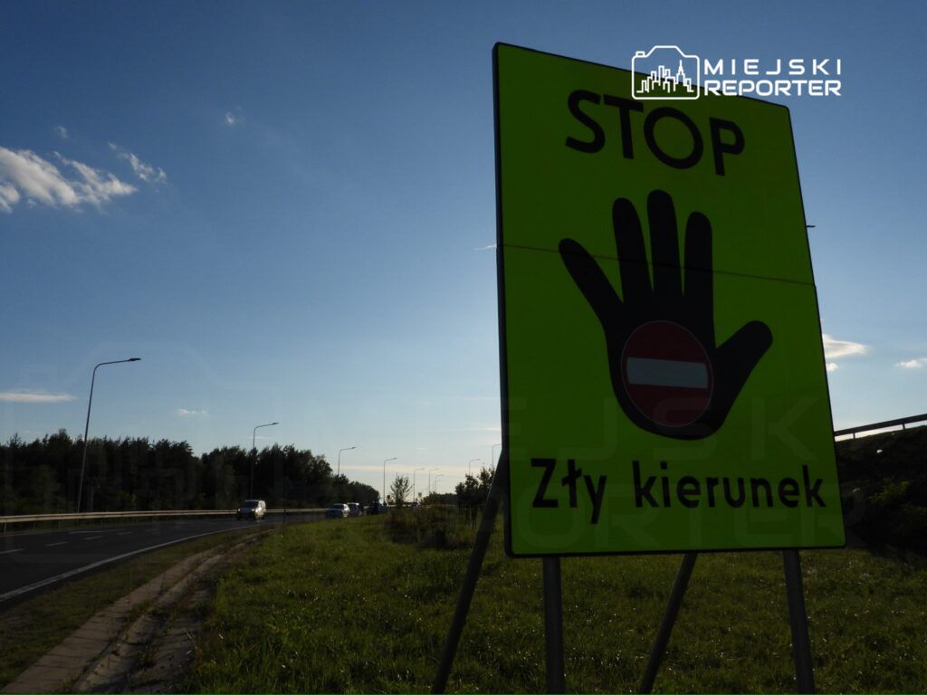 Jasnozielony znak drogowy z wyraźnym napisem "STOP" i symbolem dłoni, informujący o złym kierunku, przy drodze.