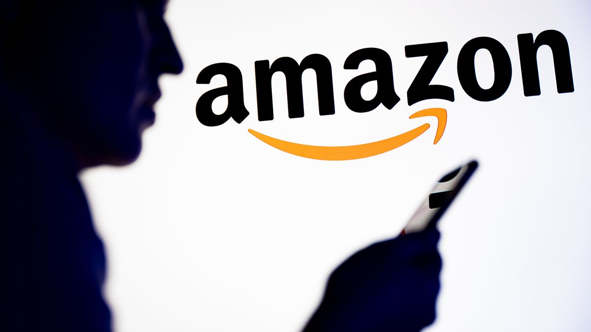 POLAND - 2025/11/26: In this photo illustration, a silhouetted individual is seen holding a mobile phone with an Amazon logo displayed in the background. (Photo Illustration by Mateusz Slodkowski/SOPA Images/LightRocket via Getty Images)