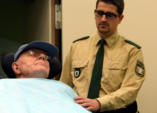 MUNICH, GERMANY - NOVEMBER 30: A German police man stands next to accused Nazi criminal John Demjanjuk (L) as he arrives at the court room on November 30, 2009 in Munich, Germany. 89 year old Demjanjuk is charged with 27,900 counts of accessory to murder for his part in the gassing of prisoners taken to Sobibor concentration camp.  (Photo by Miguel Villagran/Getty Images)