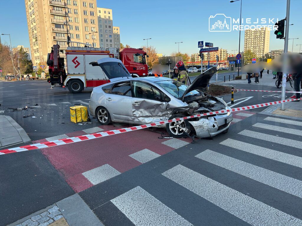 Zniszczony samochód osobowy z uszkodzoną tylną częścią stoi na przejściu dla pieszych, otoczony przez służby ratunkowe.