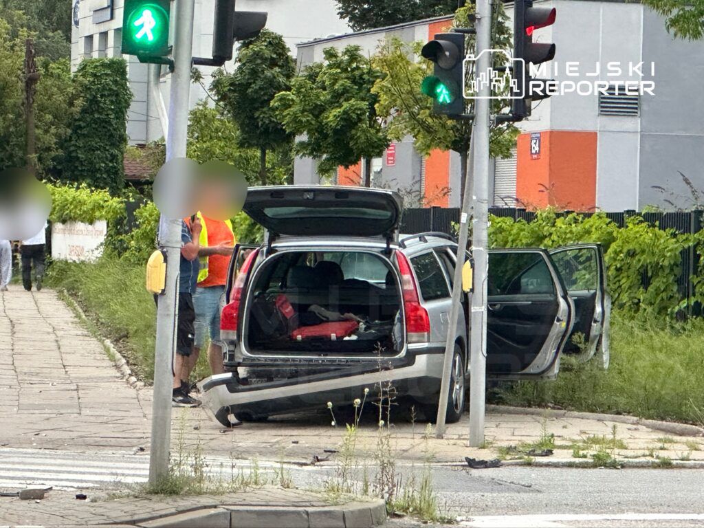 Mężczyzna w kamizelce odblaskowej rozmawia z innym mężczyzną obok otwartego bagażnika samochodu na chodniku.