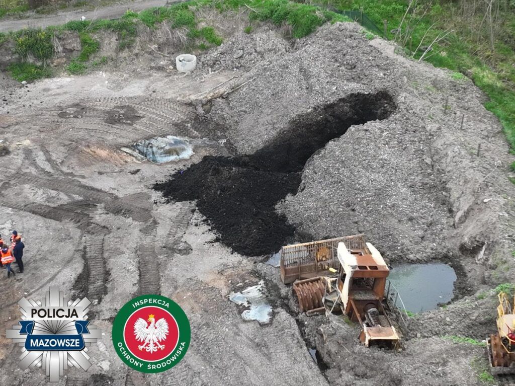 Grupa osób w odblaskowych kamizelkach bada teren wykopu, obok widoczne maszyny i nieużywane materiały.